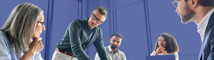 Cinco pessoas vestidas formalmente, reunidas em volta de uma mesa tendo uma reunião empresarial.