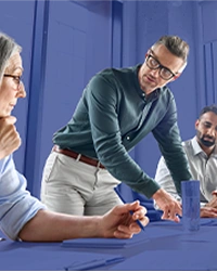 Cinco pessoas vestidas formalmente, reunidas em volta de uma mesa tendo uma reunião empresarial.